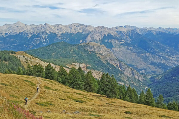 Three tiny mountain bikers in a big landscape following a narrow trail at Puy St. Vincent