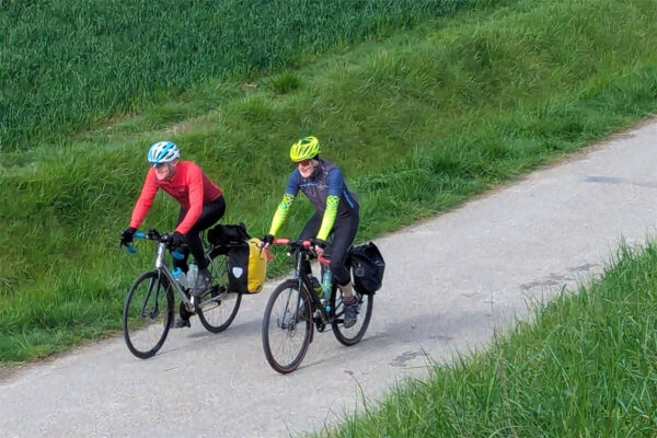 Two riders on a cycle path next to a Dutch dyke