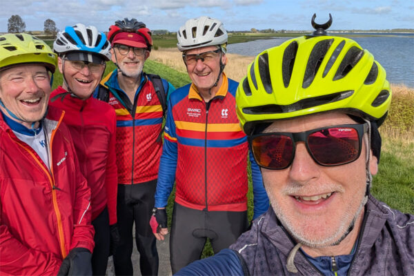 Five cyclists in mainly red tops by the Zeeland Delta shoreline