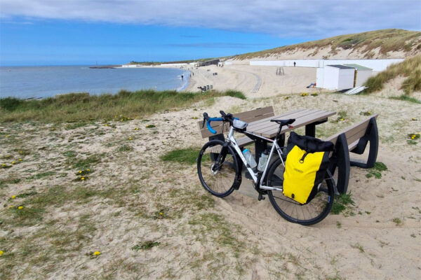 A gravel bike with pannier bag leans against a bench on the sea coast at Westkapelle