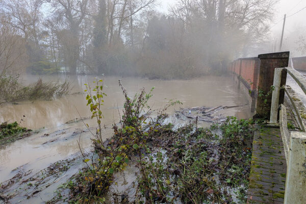 Flood waters reach the top of the arch of a road bridge over the River Mole